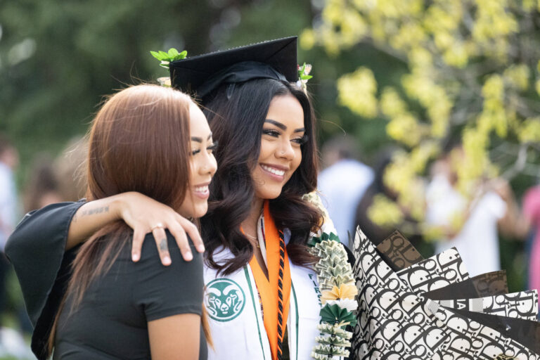 A graduate takes a photo with her friend after her ceremony with flowers in her hands.