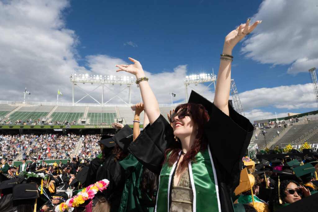 Graduates celebrate with hands raised in the sun during University-wide Commencement at Canvas Stadium.