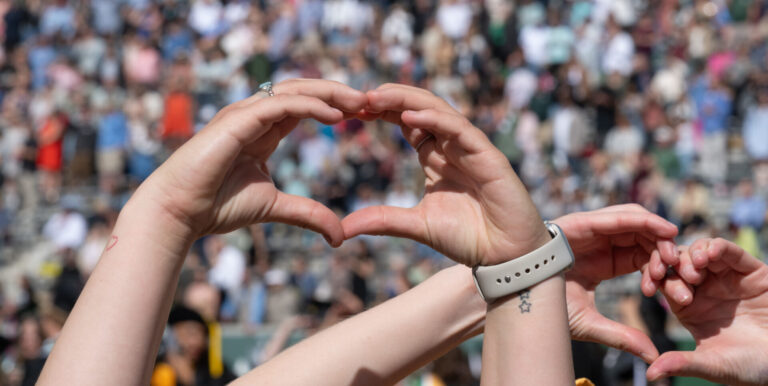 Hands making the shape of a heart stand out in the foreground of the Canvas Stadium crowd.