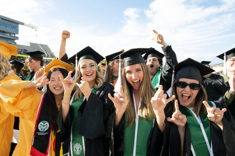 A group of graduating students celebrate and pose for a photo in Canvas Stadium.