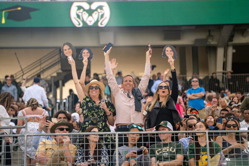 A cheering sections holding up photos of their student's face stands among the crowd at Canvas Stadium.